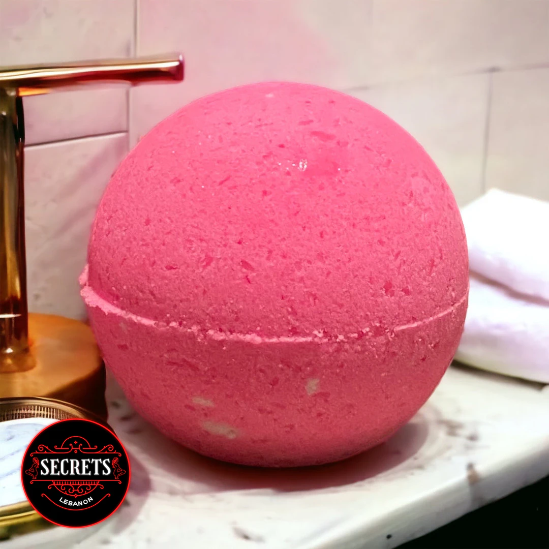 Pink Indulgence Bath Bomb resting on a marble surface near gold faucet